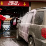 Car wash attendant applying pre-spray solution to a dirty vehicle before entering a drive in car wash tunnel